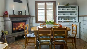 Un coin repas avec une cheminée, des chaises en bois, une table ronde et une étagère blanche où sont disposés de la vaisselle.