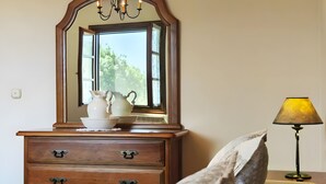 Une commode en bois avec des tiroirs et un miroir au-dessus, une lampe et une fenêtre donnant sur des arbres.
