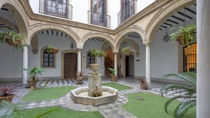 A courtyard with a fountain, potted plants, and a checkered floor.