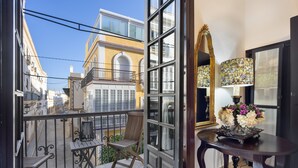 A balcony with a chair, a small table with a vase of flowers, and a view of buildings.