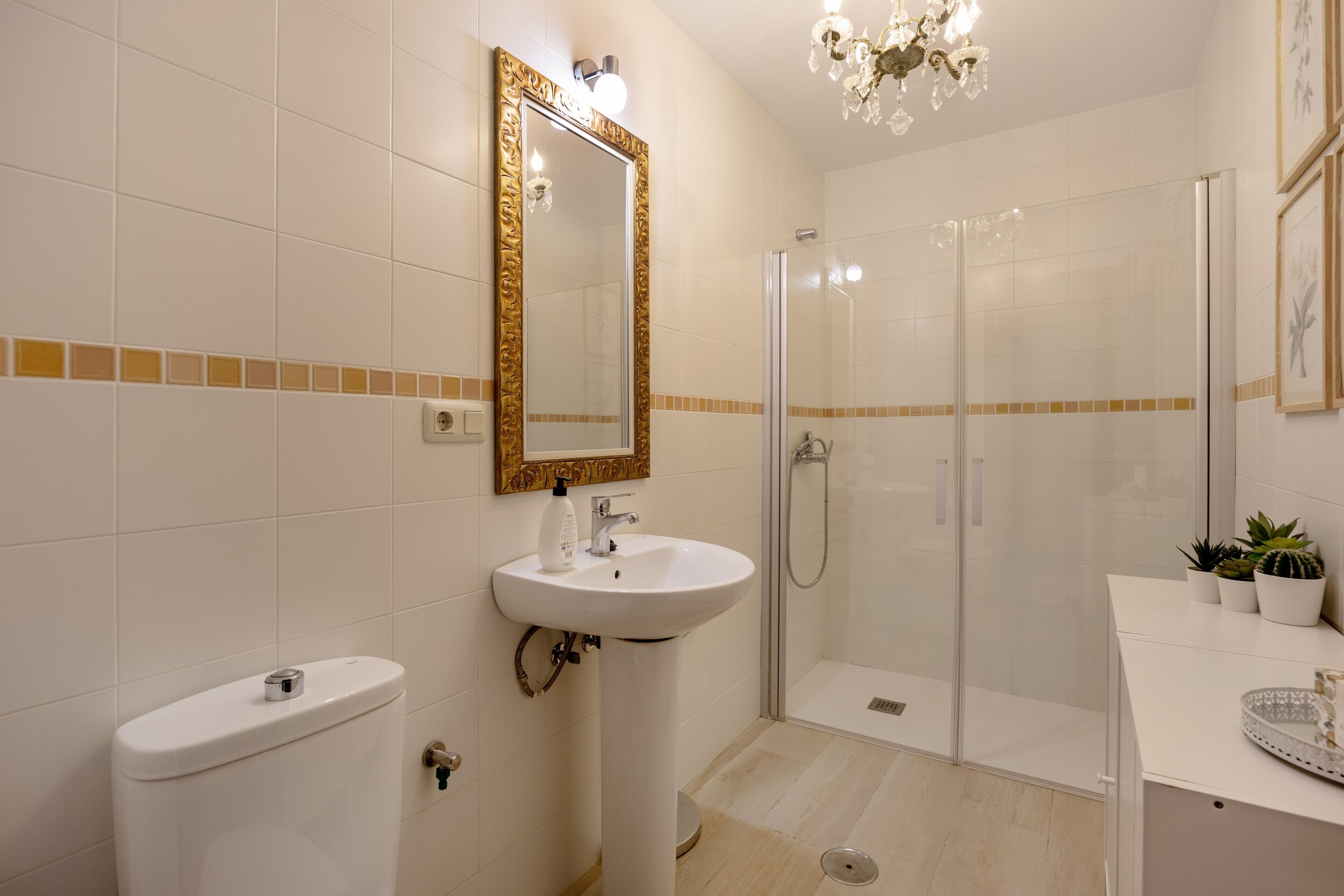A bathroom with a toilet, sink, shower, and a mirror with a decorative frame.