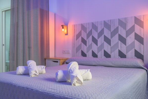 A hotel room with a bed, pillows, and a wall-mounted light.