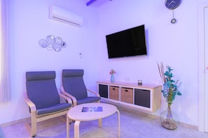 A room with two chairs, a small table, a TV, a clock, a vase with flowers, and a cabinet.