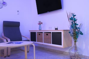 A modern room with a sofa, a small table, a TV mounted on the wall, a decorative vase, and a wooden cabinet with storage baskets.