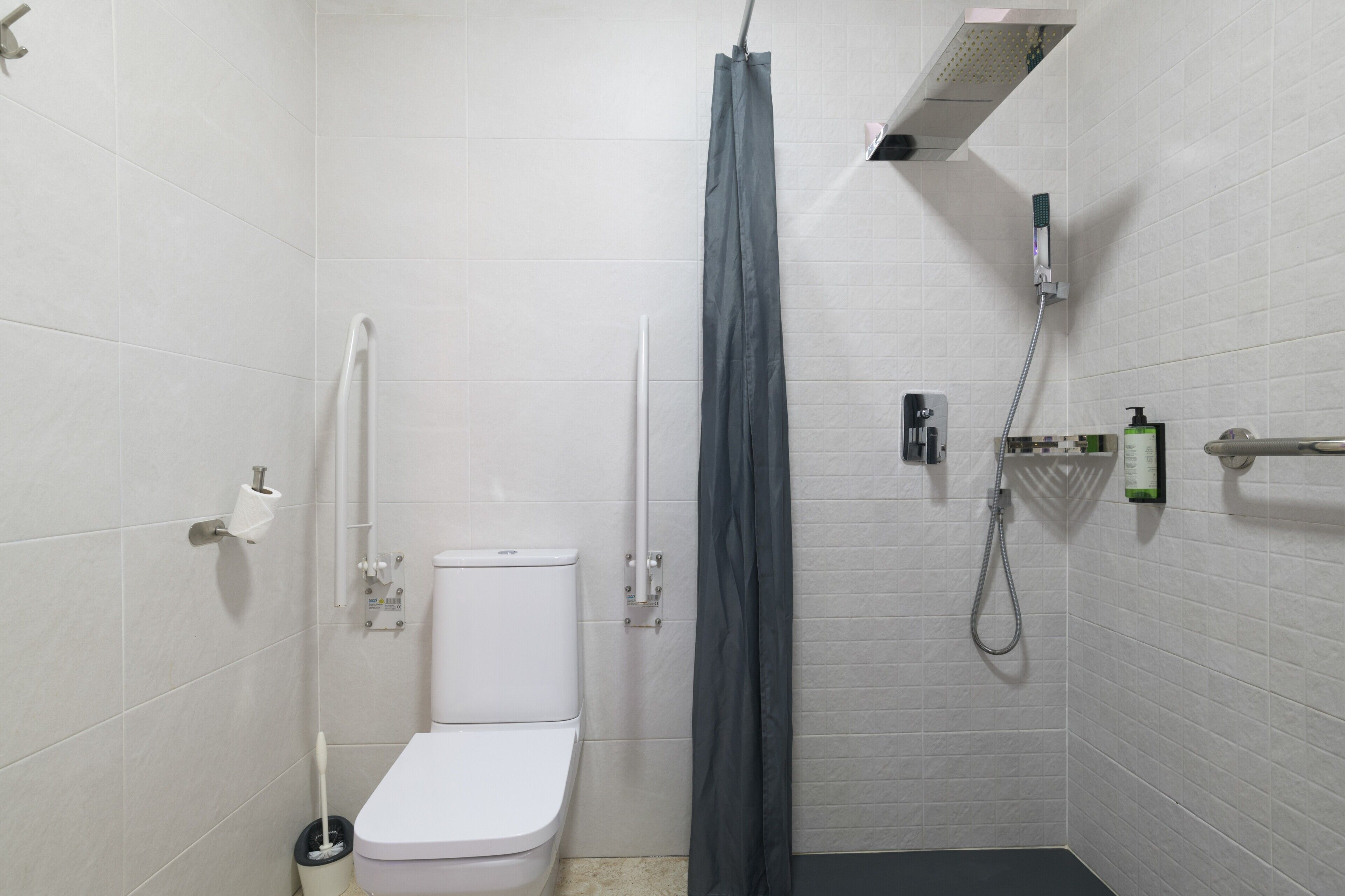 Un bagno piccolo rivestito di piastrelle bianche, con il water, una doccia e un portasciugamani.
