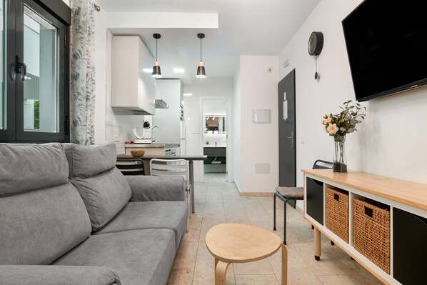 A modern living room with a grey sofa, a small wooden table, and a TV mounted on the wall.