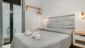 Una habitación de hotel moderna con una cama grande, un cabecero de madera, una mesita de noche pequeña y vistas a través de una puerta de cristal.