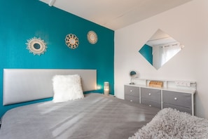 A bedroom with a bed, a nightstand, a dresser, a mirror, and wall decorations.