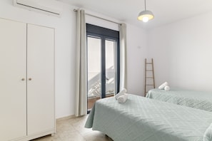 Une chambre avec deux lits, une armoire, une échelle et une vue sur l’extérieur, visible à travers une porte.
