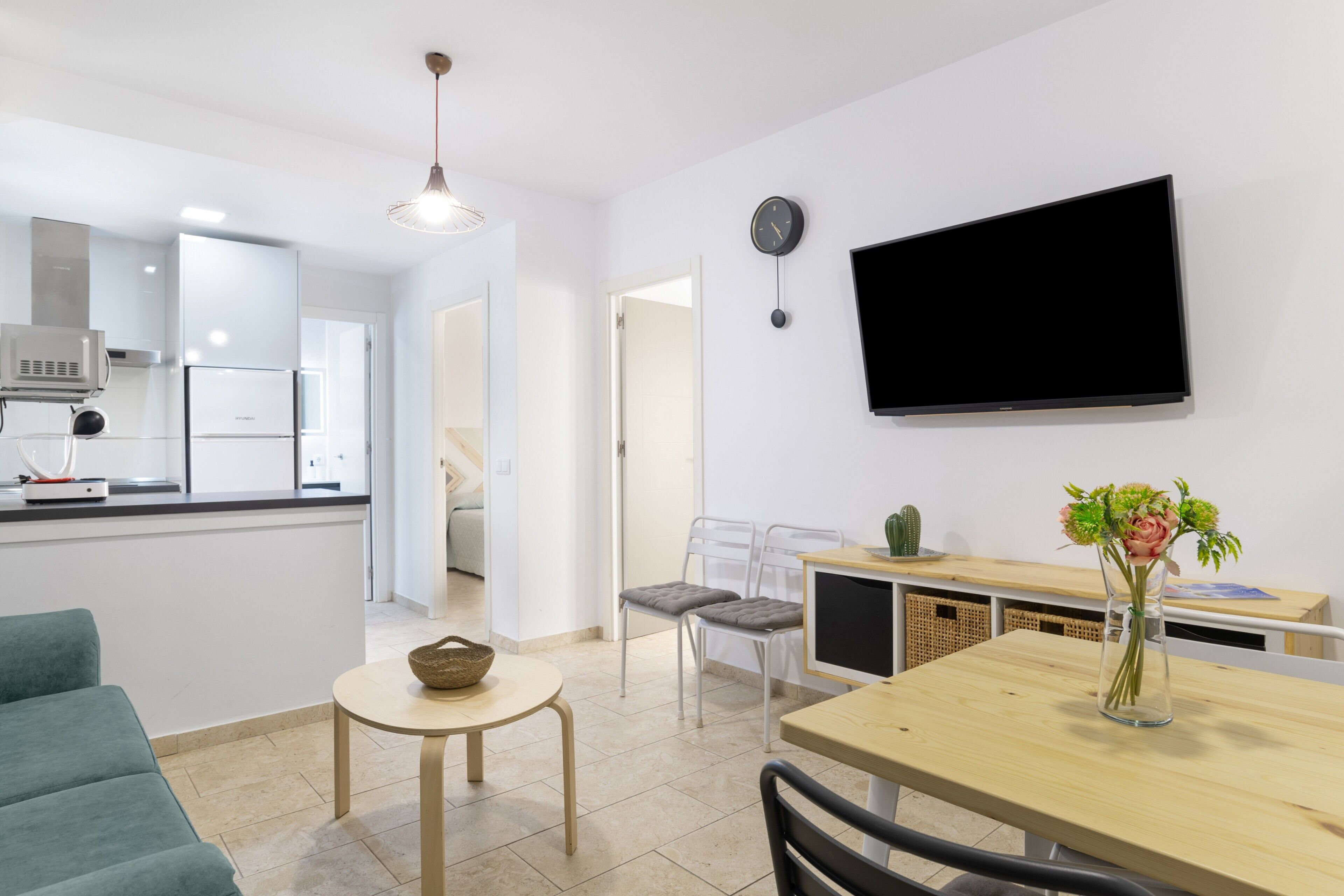 Ett modernt kök med en inbyggd ugn, en matplats med ett träbord och stolar samt en platt-TV som är monterad på väggen.