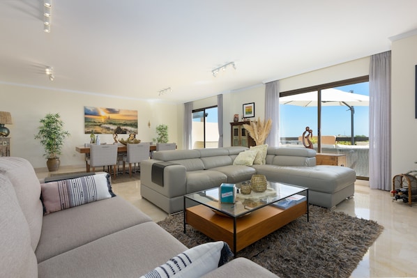 A modern living room with a sofa, a glass coffee table, and a dining area with a table and chairs.