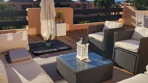 Une terrasse sur le toit, aménagée avec du mobilier d’extérieur, une table à plateau en verre et une lanterne blanche.
