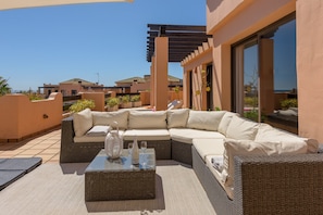 A rooftop patio with a sectional sofa, a glass-top coffee table, and a pergola.
