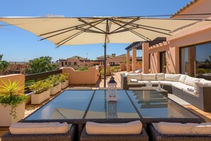 A rooftop terrace with a glass table, wicker furniture, and a large umbrella.
