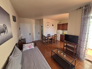 A compact living space with a sofa, a dining table, chairs, a TV, and a kitchen area.