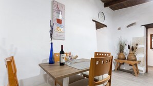 A dining area with a wooden table, chairs, a wine bottle, and a clock on the wall. - Vacation Home 'Casa Doña Carmen' with Mountain View, Private Terrace and Wi-Fi (Betancuría)
