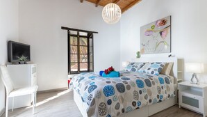 A bedroom with a bed, a chair, a TV, a window, and a painting on the wall. - Vacation Home 'Casa Doña Carmen' with Mountain View, Private Terrace and Wi-Fi (Betancuría)