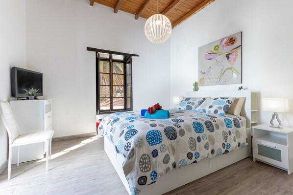 A bedroom with a bed, a chair, a TV, a window, and a painting on the wall.