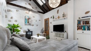 A living room with a grey sofa, a television, a bookshelf, and decorative wall elements. - Vacation Home 'Casa Doña Carmen' with Mountain View, Private Terrace and Wi-Fi (Betancuría)