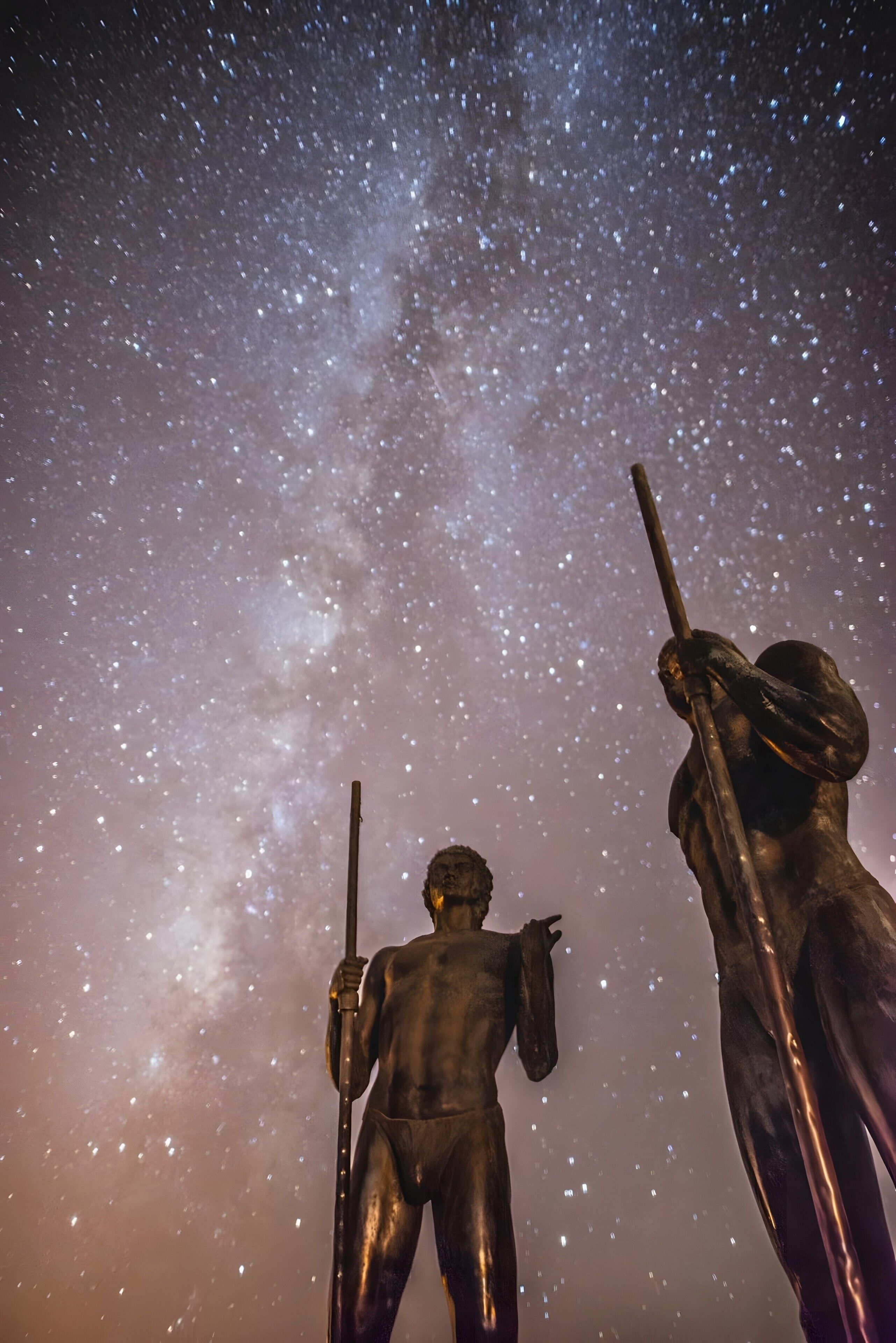 Cielo nocturno con estrellas y una estatua de una figura sosteniendo un báculo.