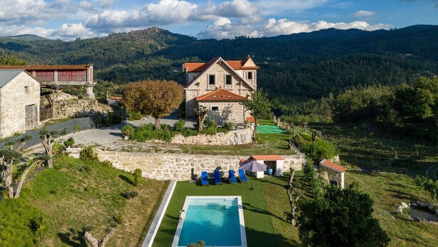 Un edificio de piedra con piscina, rodeado de vegetación y colinas.