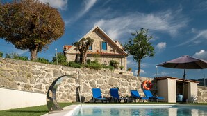 Una casa de piedra con piscina, sillas de descanso azules y un flotador.