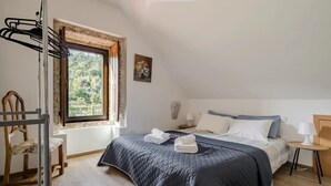Un dormitorio con una cama, una silla, un ventanal y una mesita de noche.