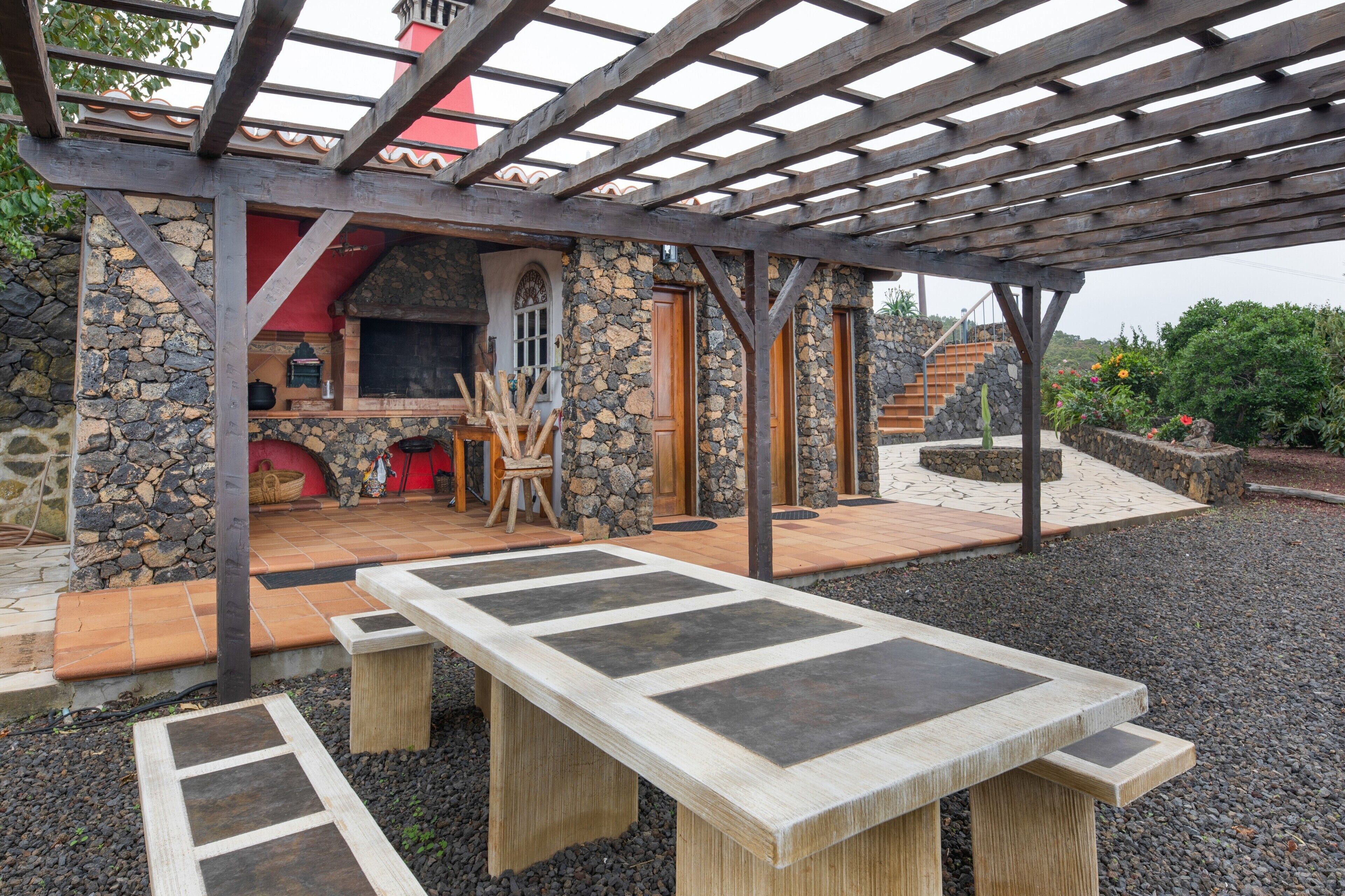 Un espacio exterior cubierto con un muro de piedra, una pérgola de madera y una zona de barbacoa.