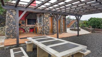 Un espacio exterior cubierto con un muro de piedra, una pérgola de madera y una zona de barbacoa.