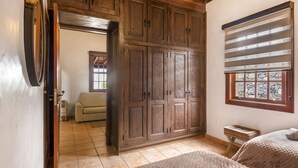 A bedroom with a wooden wardrobe, a window with blinds, a bed, and a small bedside table.