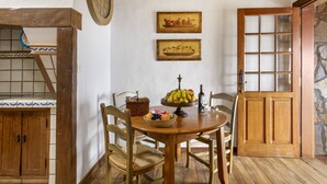 A dining area with a wooden table, chairs, a fruit bowl, and a wall clock.