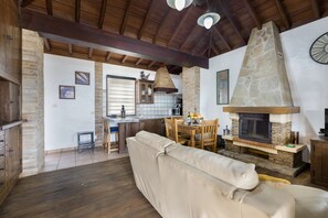 Un salon doté d’une cheminée en pierre, de poutres apparentes en bois, d’un canapé et d’un coin repas.