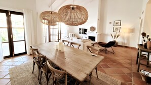 A spacious dining area with a large wooden table, several chairs, and two hanging wicker chandeliers.