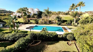 A swimming pool surrounded by lush greenery and palm trees, with a view of residential buildings in the background.