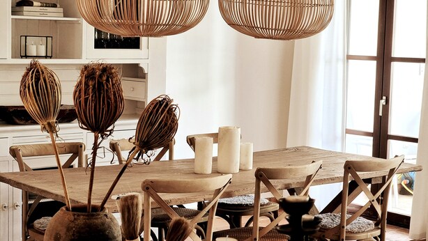 A dining area with a wooden table, wicker chairs, and hanging rattan lamps.