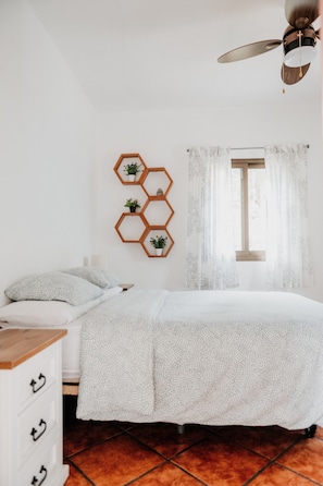 A bedroom with a bed, a dresser, a ceiling fan, a window with curtains, and a wall-mounted hexagonal shelf with plants. - Casa Rural 'Casa Rural Kiko' with Mountain Views, Private Terrace & Wi-Fi (Icod de los Vinos)