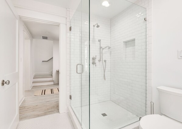 Un baño moderno con ducha de vidrio, paredes de azulejos blancos y suelo de madera.