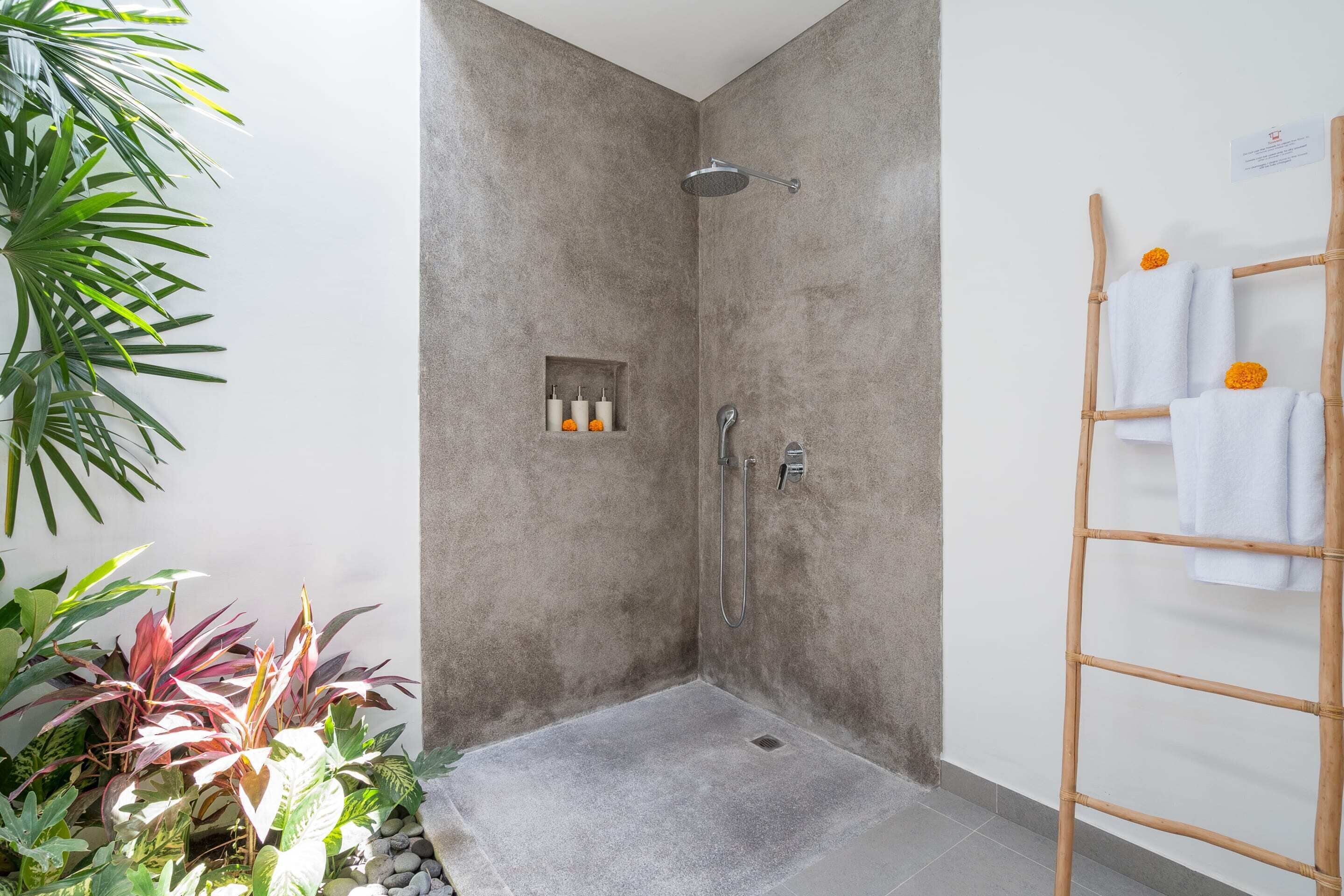 A shower area with a grey tiled floor, a bamboo towel rack, and a small shelf with toiletries.
