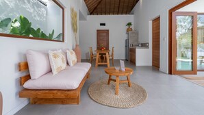 A modern interior with a wooden sofa, a round wooden table, and a large window with a view of greenery. - Villa Lounes 1 (Tabanan)