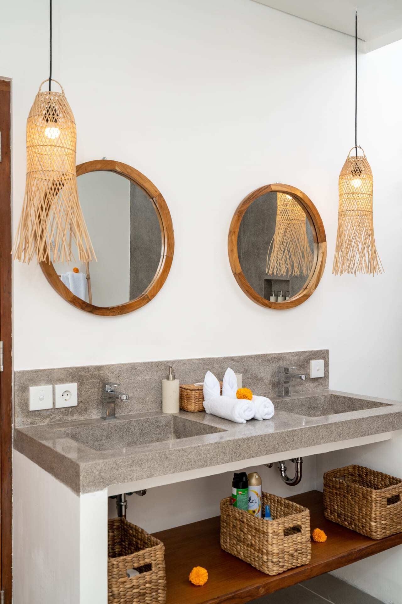 A bathroom with two round mirrors, a granite countertop, and wicker baskets under the sink.