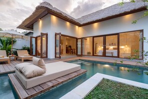Una casa moderna con piscina, terraza de madera y techo de paja.