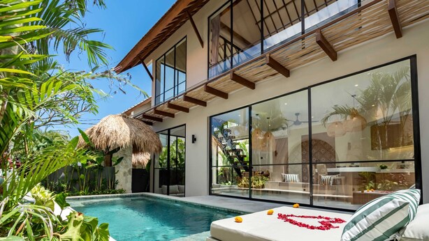 A modern poolside area with a glass-enclosed lounge, a thatched-roof structure, and lush greenery. - Villa Saya (Canggu)