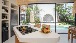A modern kitchen with a central island, built-in appliances, and a view of a pool and garden. - Villa Saya (Canggu)
