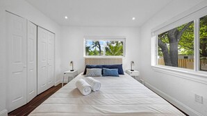 A bedroom with a large bed, two bedside tables, a window with a view of trees, and white walls.