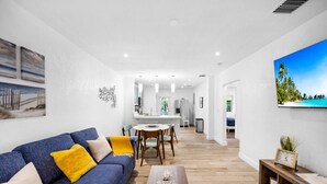 A modern living room with a blue sofa, wooden coffee table, and a dining area with a white table and chairs.