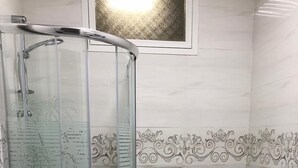 A bathroom with a glass-enclosed shower, a toilet, and a wall-mounted toilet paper holder. - Al Zahra Hotel Apartments (Ras Al Khaimah)
