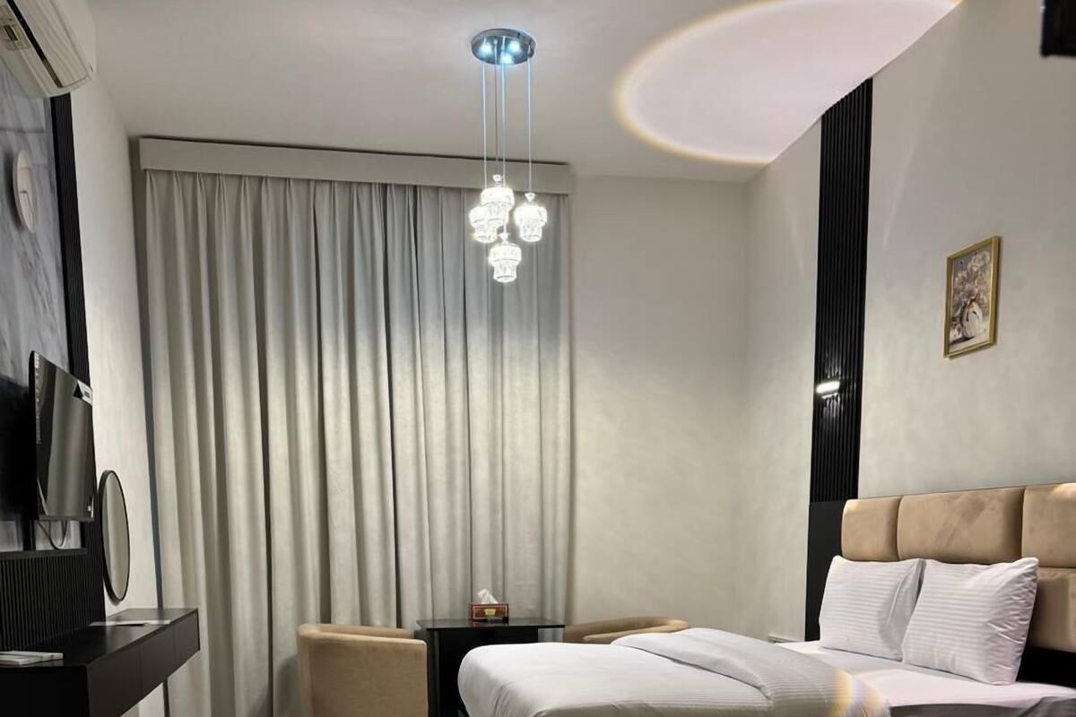 A modern hotel room with a large bed, a flat-screen TV, a bedside table, and a decorative rug.