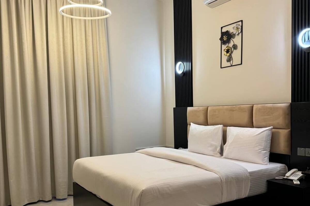 A modern bedroom with a large bed, a bedside table with a phone, an air conditioning unit, and a decorative wall piece.
