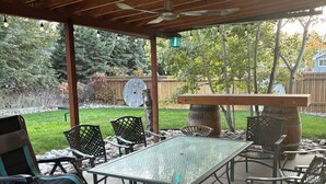 A covered patio area with a table and chairs, a ceiling fan, and a view of the backyard.