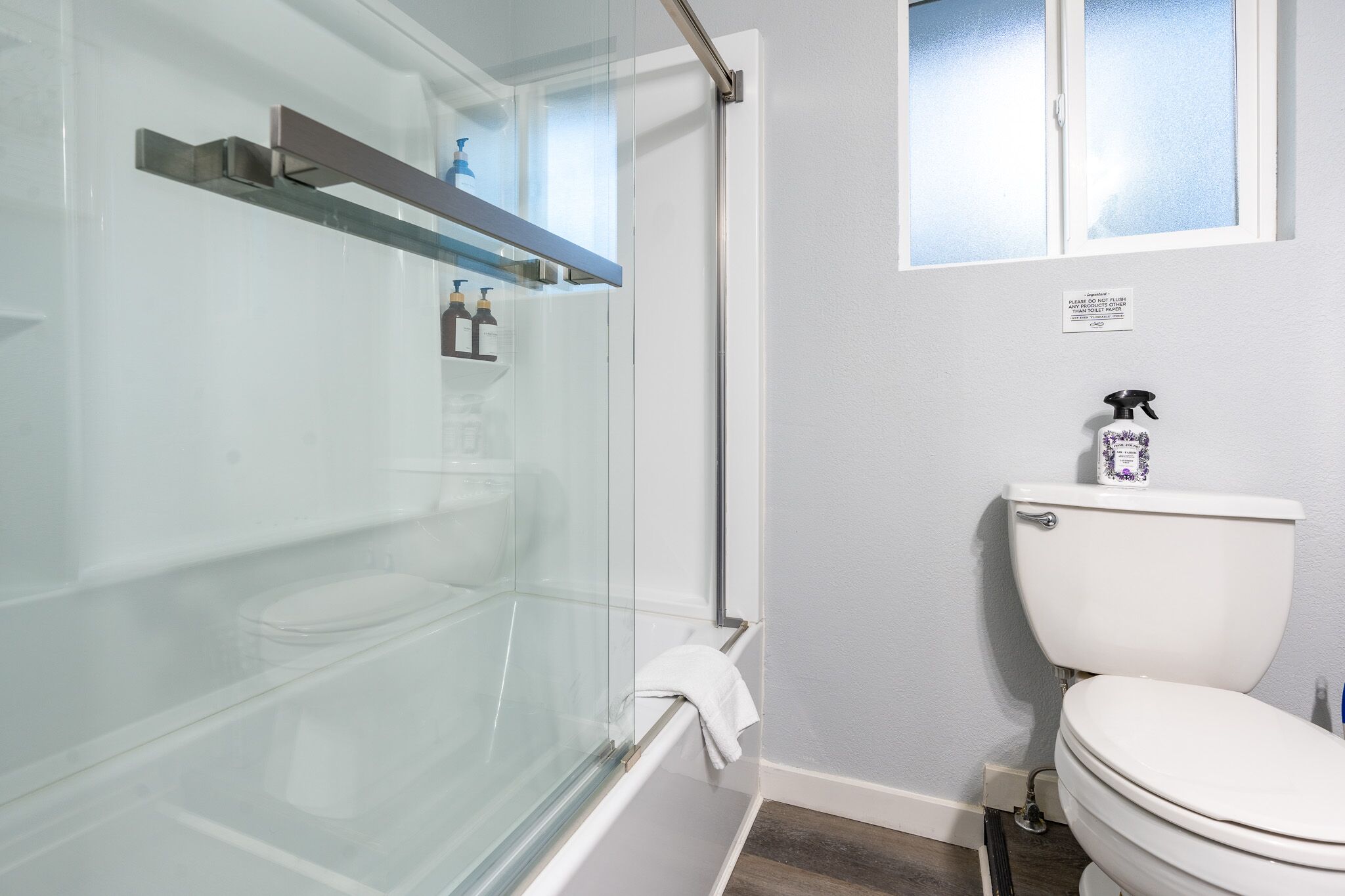 Ein Badezimmer mit Duschkabine aus Glas, Toilette und Fenster über der Toilette.